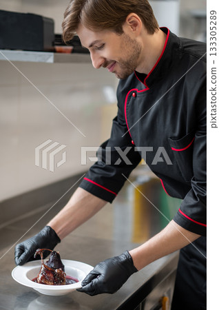 Chef holding plate with braised meat dish lamb shank or duck leg topped with sauce 133305289