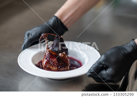 Chef in uniform holding restaurant-style dish standing in kitchen 133305290