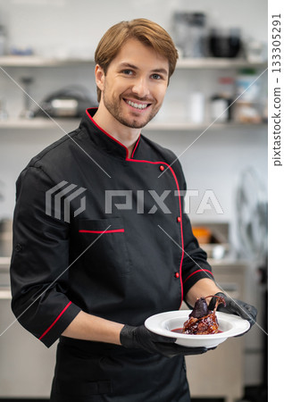 Chef in uniform holding restaurant-style dish standing in kitchen 133305291