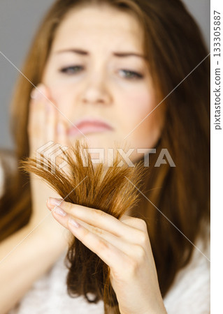 Worried woman looking at her dry hair ends Worried woman looking at her dry hair ends 133305887