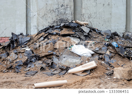 Pile of roofing felt waste against a building wall, building renovation, waste sorting, hazardous waste disposal at a construction site Pile of roofing felt waste against a building wall, building renovation, waste sorting, hazardous waste disposal at a construction site 133306451