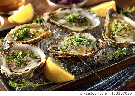 Fresh oysters on ice with herbs and lemon wedges, ready to eat 133307050