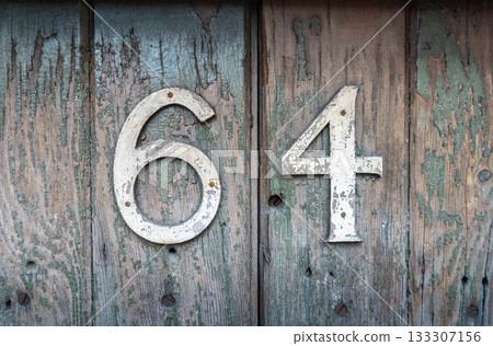 Weathered house number 64 on an old wooden surface 133307156