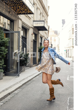 Joyful happy young adult woman wear denim jacket floral dress enjoy have fun moves playful energy urban city street show confident style warm mood. Female person carefree happiness dance outdoors Joyful happy young adult woman wear denim jacket floral dress enjoy have fun moves playful energy urban city street show confident style warm mood. Female person carefree happiness dance outdoors 133307540