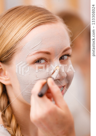 Woman applying with brush clay mud mask to her face Woman applying with brush clay mud mask to her face 133308024