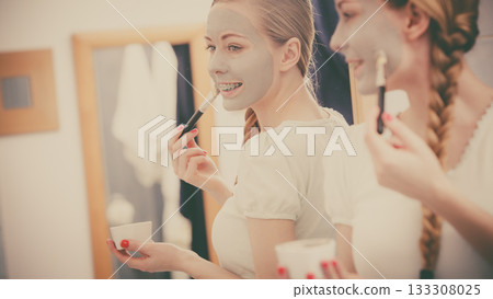 Happy young woman applying mud mask on face Happy young woman applying mud mask on face 133308025