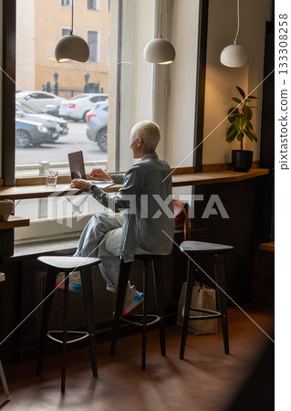 African American woman with short blond hair is sitting at a table, typing on laptop. 133308258