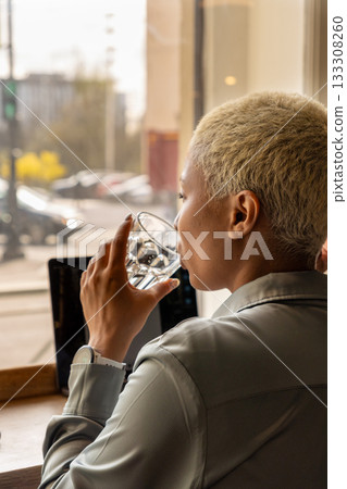 African American woman with short blond hair is sitting at a table, typing on laptop. 133308260
