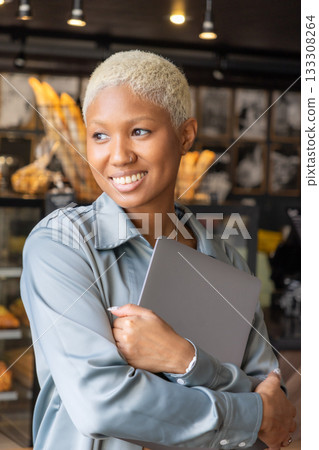 African American woman with short blond hair smiles and holds laptop in her hands. African American woman with short blond hair smiles and holds laptop in her hands. 133308264