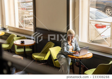 African American woman with white hair sits at desk with laptop, is surfing the Internet. female blogger. African American woman with white hair sits at desk with laptop, is surfing the Internet. female blogger. 133308288