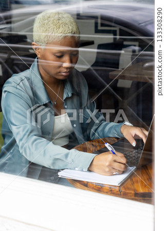 African American woman with short blond hair sits at table and types on laptop. African American woman with short blond hair sits at table and types on laptop. 133308290