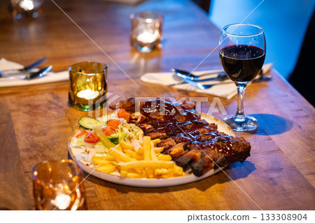 Tender grilled porterhouse or t-bone steak served with crisp golden French fries and fresh green herb salad accompanied by a BBQ or tomato ketchup sauce 133308904
