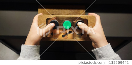 A child's hands grip a small wooden control panel with three buttons. Concepts include child development, tactile learning, technology for children, hand-eye coordination, and interactive exhibits. A child's hands grip a small wooden control panel with three buttons. Concepts include child development, tactile learning, technology for children, hand-eye coordination, and interactive exhibits. 133309441