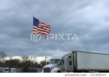 Large American flag waves above parked truck near truck stop location Large American flag waves above parked truck near truck stop location 133309547