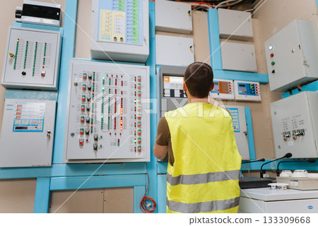 Technician checking control panels with indicator lights in industrial control room Technician checking control panels with indicator lights in industrial control room 133309668