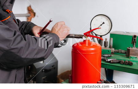 Technician refilling red fire extinguisher during pressure testing at workshop, close up Technician refilling red fire extinguisher during pressure testing at workshop, close up 133309671