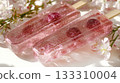 3D rendering glass transparent pink ice popsicle cherries frozen inside, placed textured surface surrounded blooming cherry blossoms 133310004