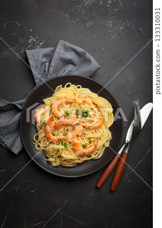 Spaghetti pasta shrimps parsley lemon seafood meal black plate dark background 133310031