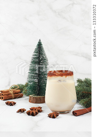 Eggnog with cinnamon, star anise, and nutmeg for Christmas and the winter holidays on a marble table with fir branches. A warming eggnog during the cold season, a festive arrangement for Christmas Eve Eggnog with cinnamon, star anise, and nutmeg for Christmas and the winter holidays on a marble table with fir branches. A warming eggnog during the cold season, a festive arrangement for Christmas Eve 133310372