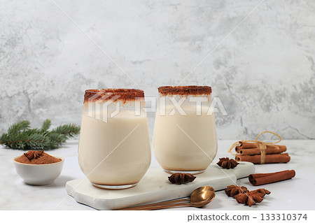 Eggnog with cinnamon, star anise, and nutmeg for Christmas and the winter holidays on a marble table with fir branches. A warming eggnog during the cold season, a festive arrangement for Christmas Eve Eggnog with cinnamon, star anise, and nutmeg for Christmas and the winter holidays on a marble table with fir branches. A warming eggnog during the cold season, a festive arrangement for Christmas Eve 133310374