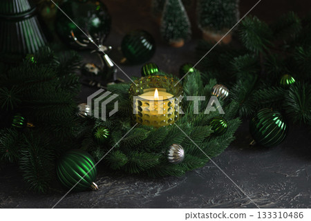 Lit Candle in Green Glass Holder with Pine Wreath and Christmas Ornaments Lit Candle in Green Glass Holder with Pine Wreath and Christmas Ornaments 133310486