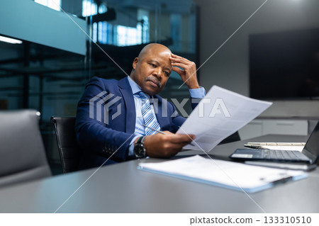 Serious mature African American businessman analyzing documents in modern office Serious mature African American businessman analyzing documents in modern office 133310510