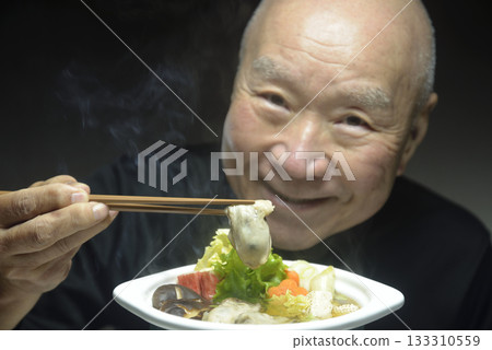 一位老人面帶微笑地吃著熱氣騰騰的蚵仔火鍋。 133310559