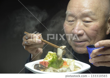 An elderly man eating hot oyster hotpot with a smile 133310565