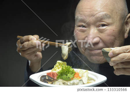 An elderly man eating hot oyster hotpot with a smile 133310566