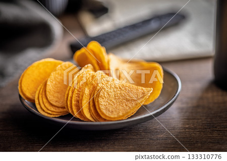 Crispy potato chips on plate on wooden table. Crispy potato chips on plate on wooden table. 133310776