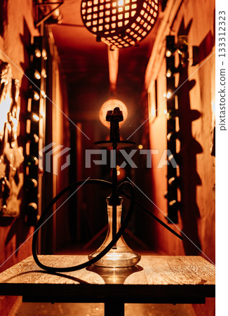 Hookah silhouette on wooden table under warm lights in moody lounge corridor Hookah silhouette on wooden table under warm lights in moody lounge corridor 133312323