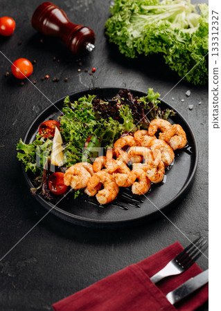 Grilled shrimp salad with mixed greens, cherry tomatoes and lemon on a black plate Grilled shrimp salad with mixed greens, cherry tomatoes and lemon on a black plate 133312327