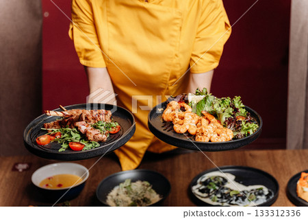Chef presenting shrimp salad and grilled ribs on black plates in a modern restaurant 133312336