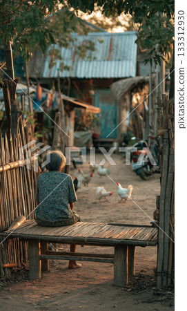 Elderly woman sitting on wooden bench in peaceful rural Thai village at sunset, surrounded by chickens and rustic houses, tranquil atmosphere 133312930