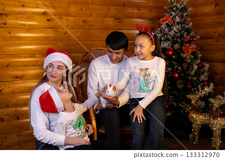 family celebrates Christmas around a decorated Christmas tree and pet a rabbit 133312970