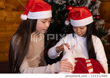 girls are interacting with a small white rabbit on a red Christmas-themed pillow girls are interacting with a small white rabbit on a red Christmas-themed pillow 133312988