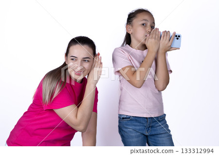 A woman is listening intently while a girl speaks into a phone A woman is listening intently while a girl speaks into a phone 133312994
