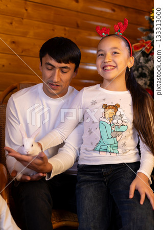 family celebrates Christmas around a decorated Christmas tree and pet a rabbit family celebrates Christmas around a decorated Christmas tree and pet a rabbit 133313000