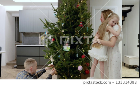Smiling parents and child hanging ornaments, arranging twinkling lights on christmas tree, sharing warm seasonal moments together at home Smiling parents and child hanging ornaments, arranging twinkling lights on christmas tree, sharing warm seasonal moments together at home 133314398