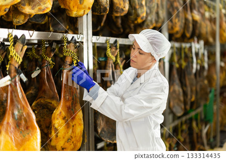 female worker checks the quality of jamon in a factory 133314435