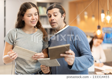 Couple of man and woman choosing sample of laminate flooring in hardware store Couple of man and woman choosing sample of laminate flooring in hardware store 133314455
