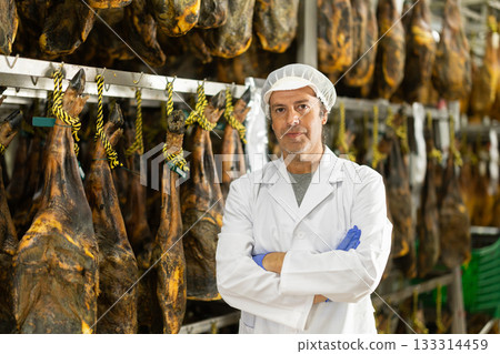 Man employee in white uniform, bathrobe and hat, stands in workshop for production of hamon 133314459