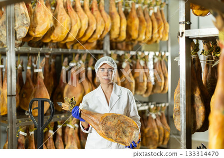 In jamon production shop, woman employee demonstrates final product 133314470