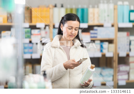 Middle-aged woman scanning QR-code on shampoo in drugstore Middle-aged woman scanning QR-code on shampoo in drugstore 133314611