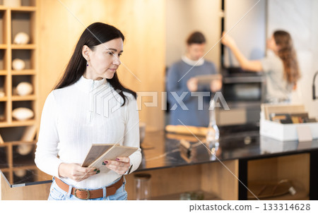 Female shopper carefully selects samples of material for a future kitchen set in furniture store 133314628