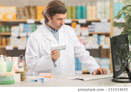 Male pharmacist looking for pills on computer 133314655