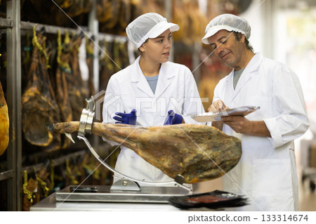 woman and a man workers stand near the jamon and check the quality woman and a man workers stand near the jamon and check the quality 133314674