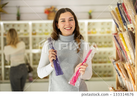 Girl client chooses aroma sticks, inhales fragrance, woman shopping in background Girl client chooses aroma sticks, inhales fragrance, woman shopping in background 133314676