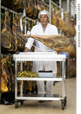 Man employee of hamon manufacturing workshop presents product using jamonero 133314684