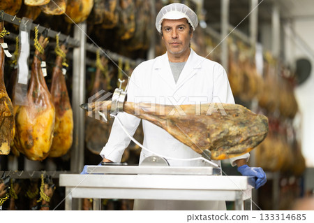 Man employee of hamon manufacturing workshop presents product using jamonero 133314685